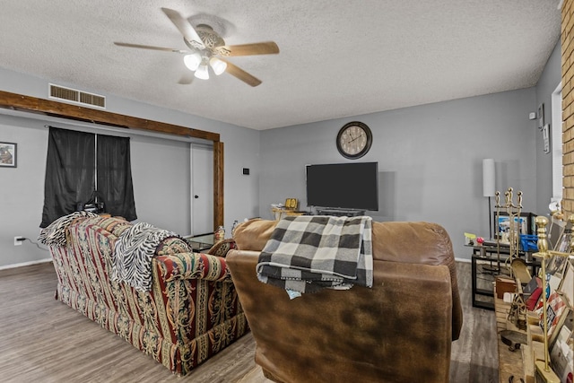 living room with ceiling fan, a textured ceiling, and light wood-type flooring