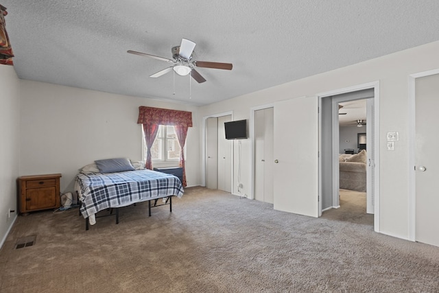 carpeted bedroom featuring ceiling fan, a textured ceiling, and multiple closets