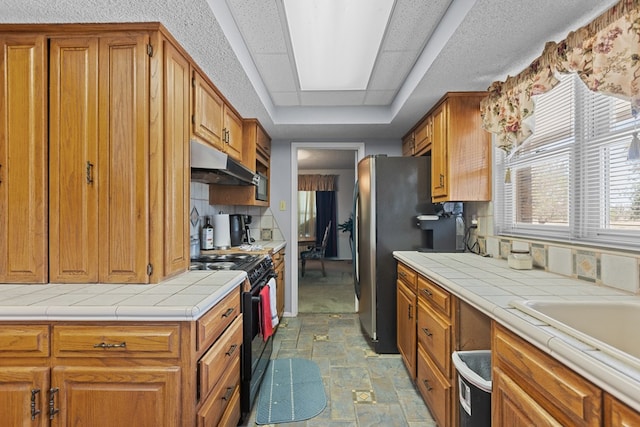 kitchen with tile counters, stainless steel fridge, decorative backsplash, and black / electric stove