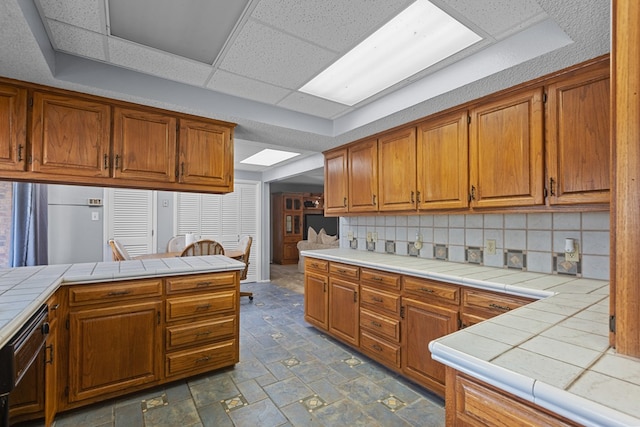 kitchen featuring tile counters, a drop ceiling, kitchen peninsula, and backsplash