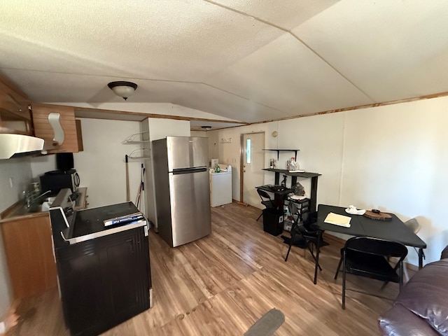 kitchen with appliances with stainless steel finishes, a textured ceiling, washer / dryer, vaulted ceiling, and light wood-type flooring