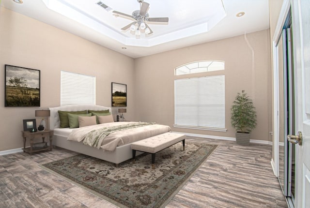 bedroom with wood-type flooring, a tray ceiling, and ceiling fan