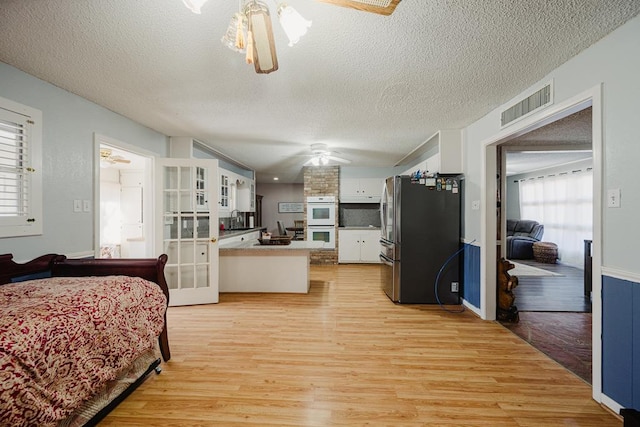 bedroom with light wood-type flooring, a textured ceiling, french doors, stainless steel fridge, and sink