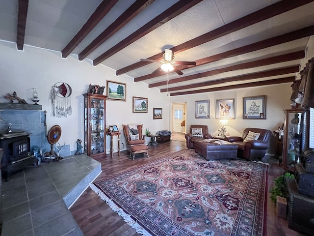 living room featuring ceiling fan, dark wood-type flooring, a wood stove, and beam ceiling