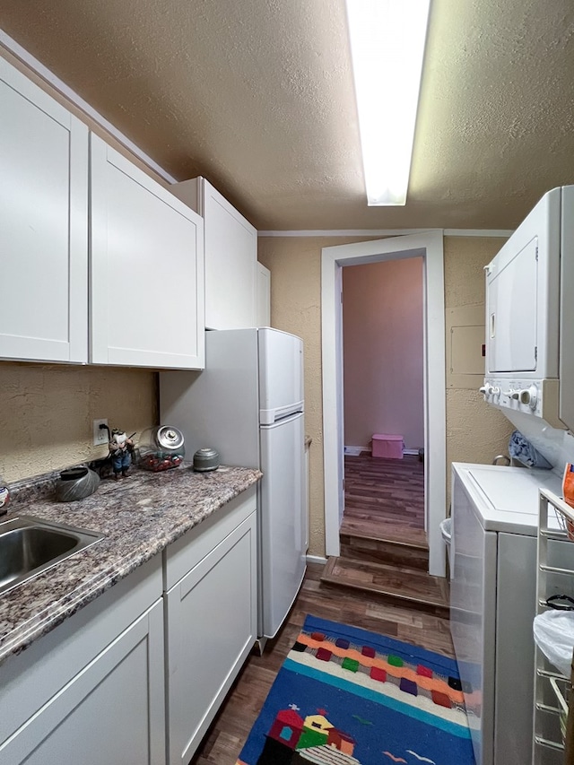 kitchen featuring stacked washing maching and dryer, dark hardwood / wood-style flooring, a textured ceiling, white cabinets, and sink