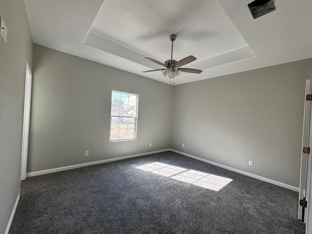 spare room with dark carpet, baseboards, a raised ceiling, and a ceiling fan