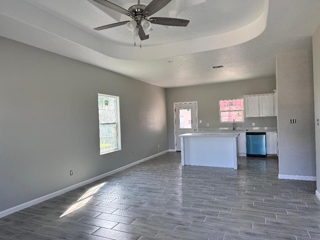 kitchen with open floor plan, white cabinets, a sink, dishwasher, and baseboards