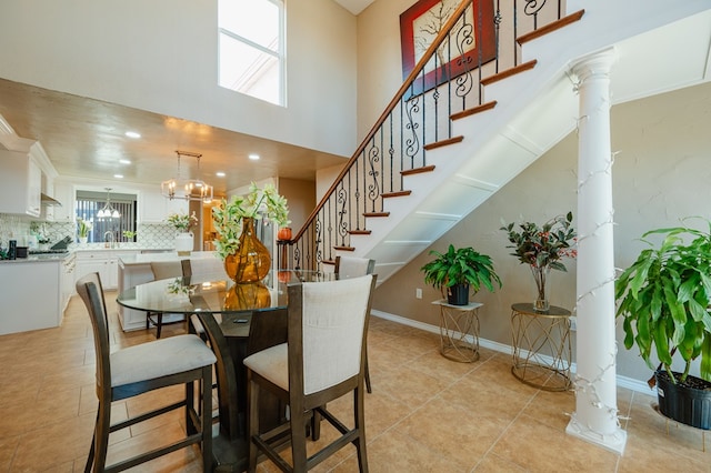 tiled dining area featuring ornate columns, crown molding, sink, a chandelier, and a high ceiling