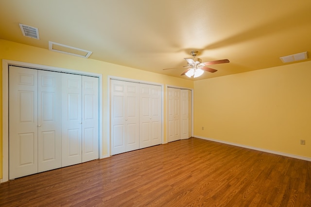 unfurnished bedroom with hardwood / wood-style floors, ceiling fan, and two closets