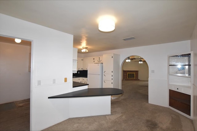 kitchen with white cabinets, dark colored carpet, a fireplace, white fridge, and kitchen peninsula