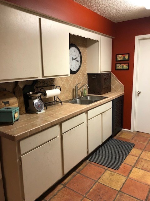 kitchen featuring decorative backsplash, tile countertops, white cabinetry, and sink