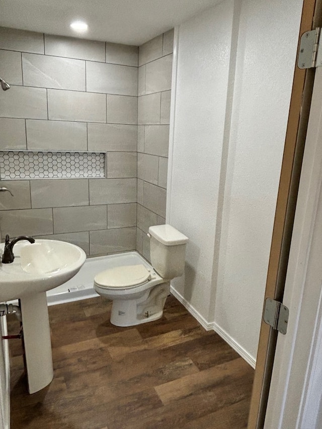 bathroom with hardwood / wood-style floors, toilet, and a tile shower