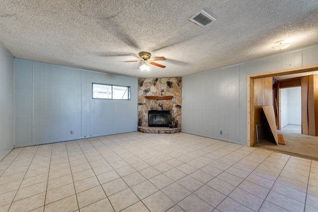 unfurnished living room with light tile patterned floors, ceiling fan, wooden walls, a fireplace, and a textured ceiling