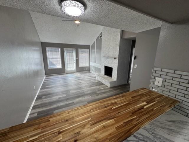 unfurnished living room with a textured ceiling, vaulted ceiling, ceiling fan, wood-type flooring, and a fireplace