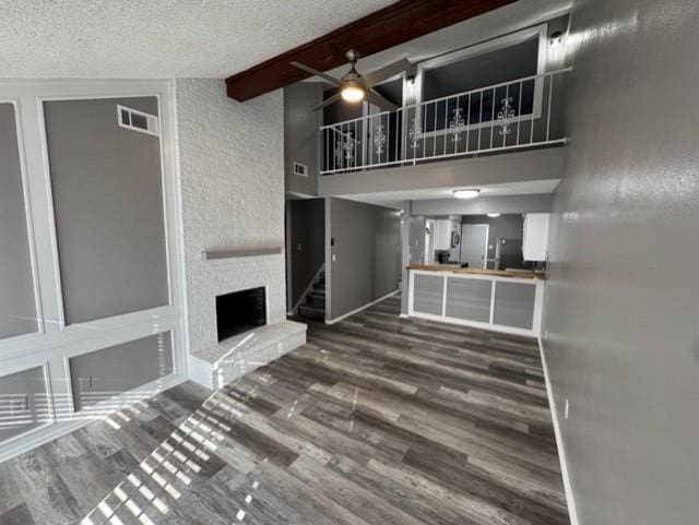 unfurnished living room featuring a textured ceiling, ceiling fan, beam ceiling, wood-type flooring, and a fireplace