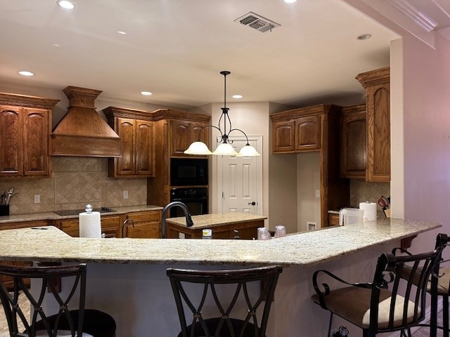 kitchen with custom exhaust hood, visible vents, backsplash, a kitchen island, and black appliances