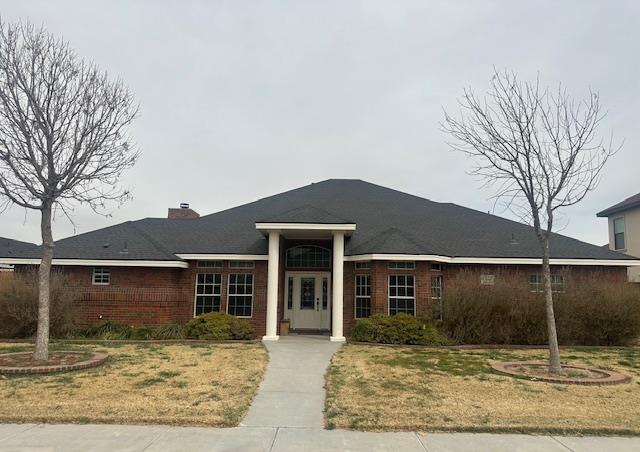 ranch-style house with brick siding, a chimney, and a front lawn