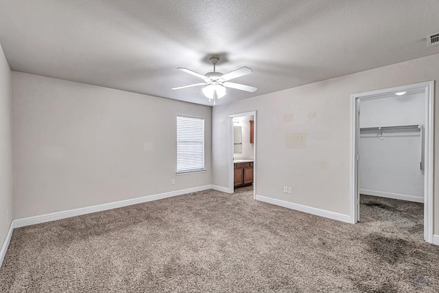 unfurnished bedroom featuring a spacious closet, carpet floors, a closet, and ceiling fan