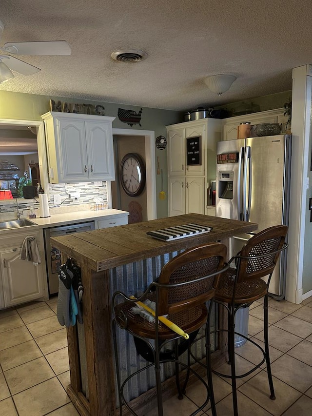 kitchen featuring light tile patterned floors, stainless steel fridge, and white cabinets