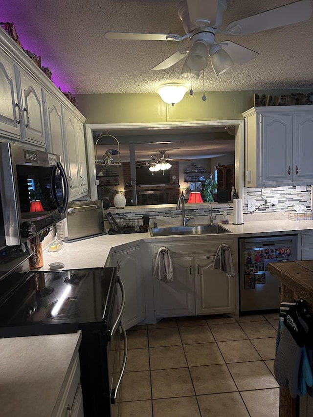 kitchen with light tile patterned floors, dishwashing machine, stainless steel microwave, a textured ceiling, and a sink