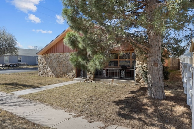 rear view of house featuring stone siding, board and batten siding, and fence