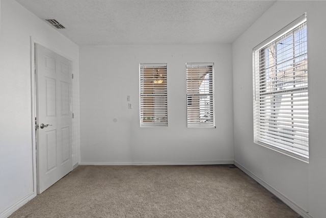 spare room with baseboards, visible vents, light carpet, and a textured ceiling