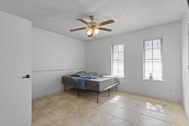 bedroom featuring a ceiling fan, a textured ceiling, baseboards, and tile patterned floors