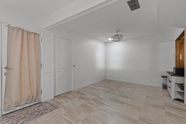 interior space featuring baseboards, a textured ceiling, visible vents, and a ceiling fan