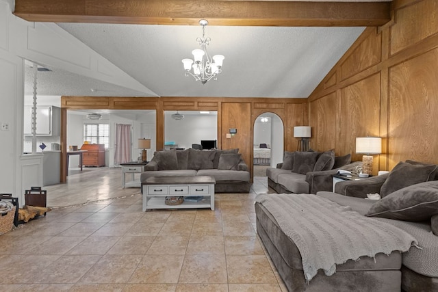 living room featuring arched walkways, lofted ceiling with beams, wood walls, a chandelier, and light tile patterned flooring