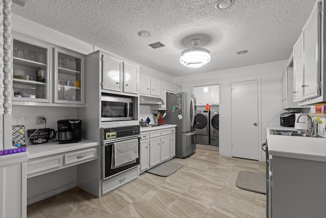 kitchen featuring washing machine and clothes dryer, light countertops, appliances with stainless steel finishes, a sink, and under cabinet range hood