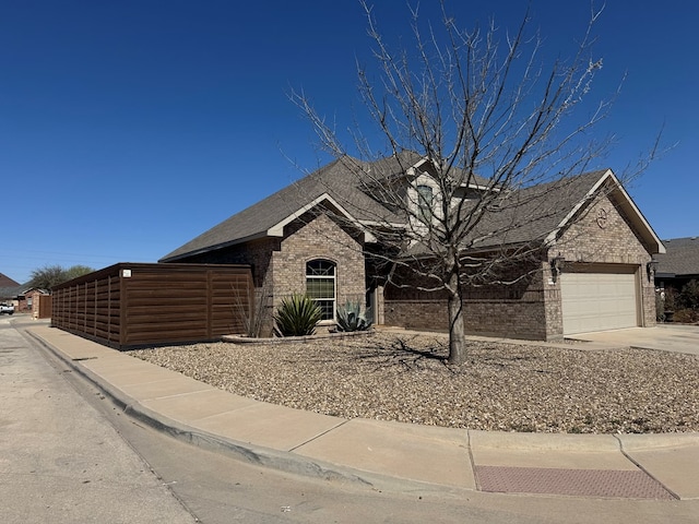 view of front of house featuring driveway, fence, roof with shingles, a garage, and brick siding