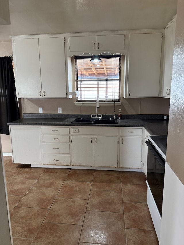 kitchen featuring tile patterned floors, electric range, a sink, dark countertops, and white cabinetry