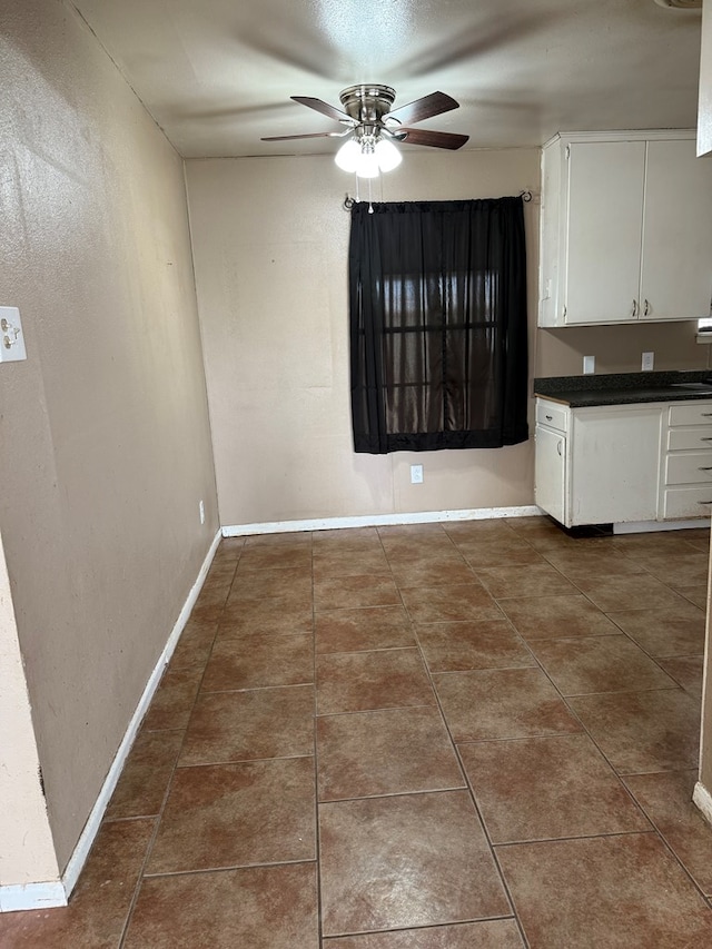 unfurnished dining area with dark tile patterned floors, baseboards, and a ceiling fan