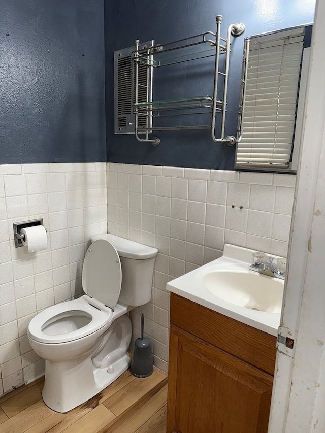 bathroom featuring vanity, wood finished floors, wainscoting, tile walls, and toilet