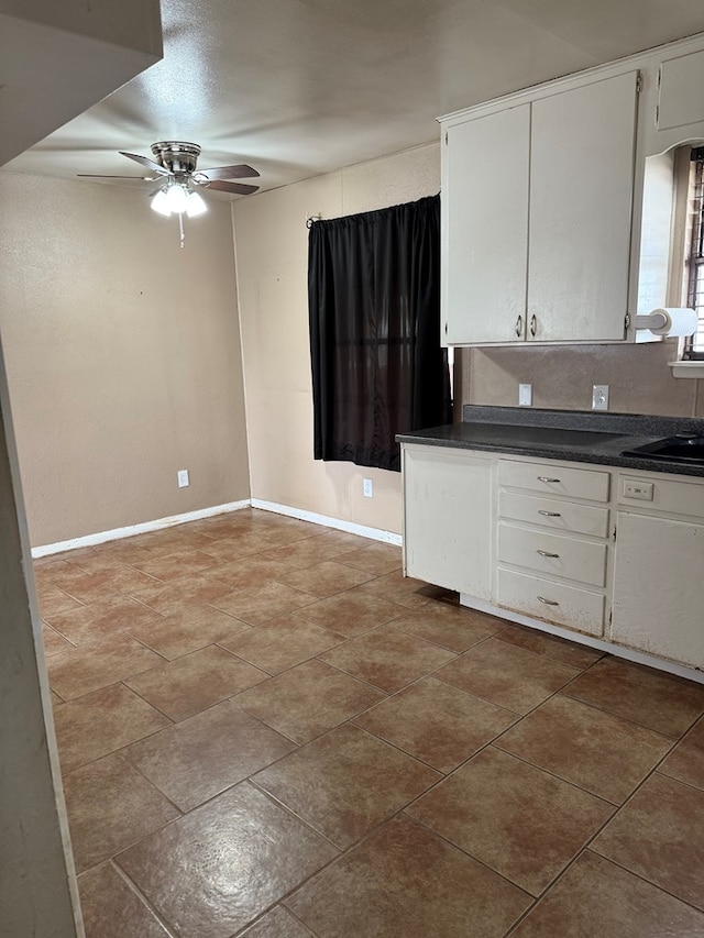 kitchen featuring a ceiling fan, a sink, dark countertops, white cabinetry, and baseboards