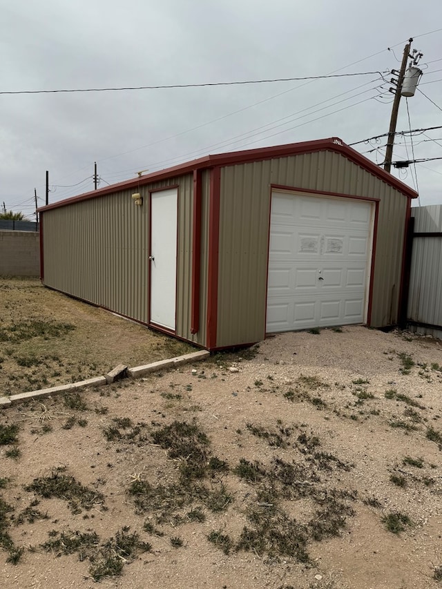 detached garage featuring dirt driveway and fence