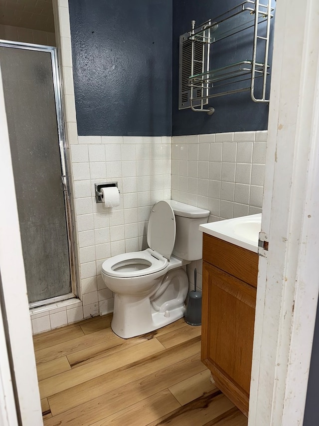 bathroom featuring toilet, a stall shower, wood finished floors, tile walls, and vanity