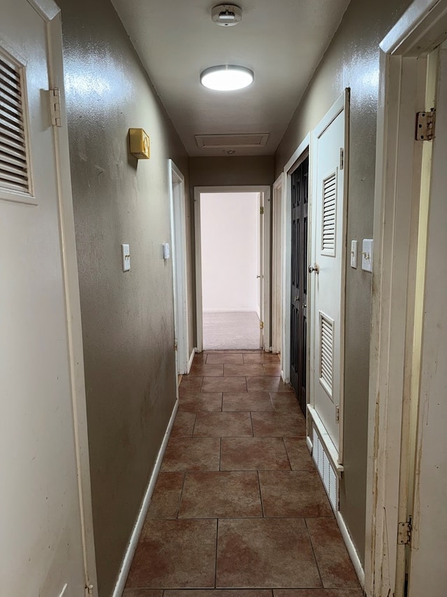 corridor featuring tile patterned flooring, attic access, a textured wall, and baseboards