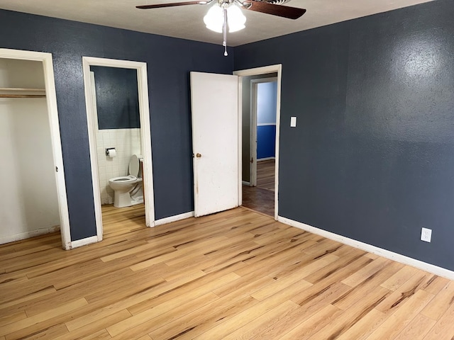 unfurnished bedroom with a ceiling fan, ensuite bath, wood finished floors, a closet, and tile walls