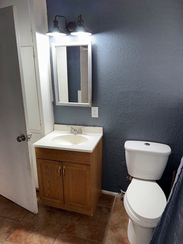 bathroom with tile patterned floors, toilet, vanity, and a textured wall