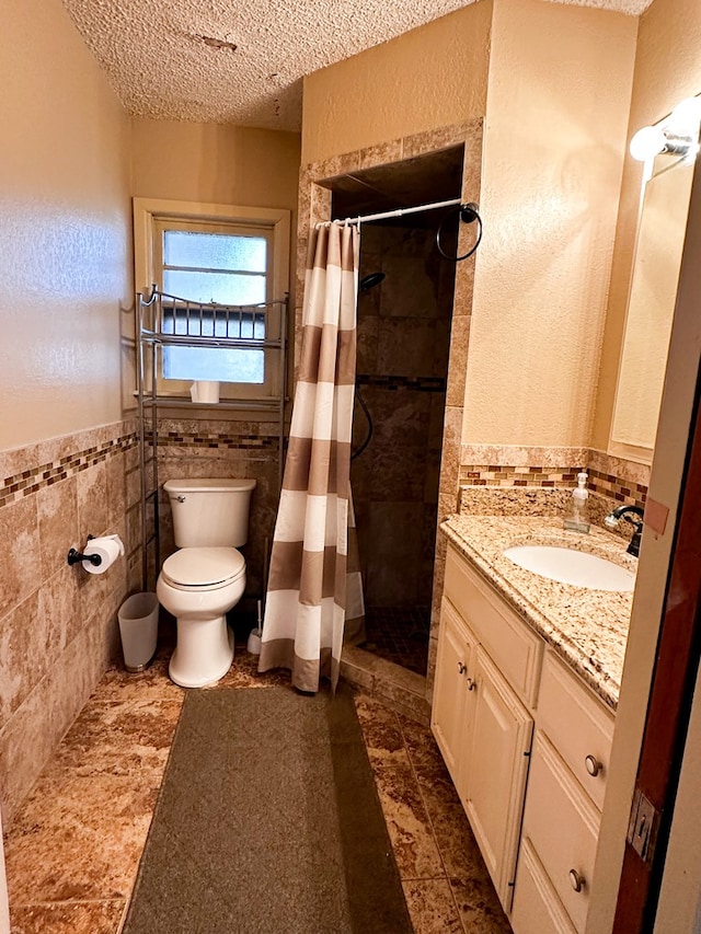 bathroom with tile walls, a shower with shower curtain, vanity, a textured ceiling, and toilet