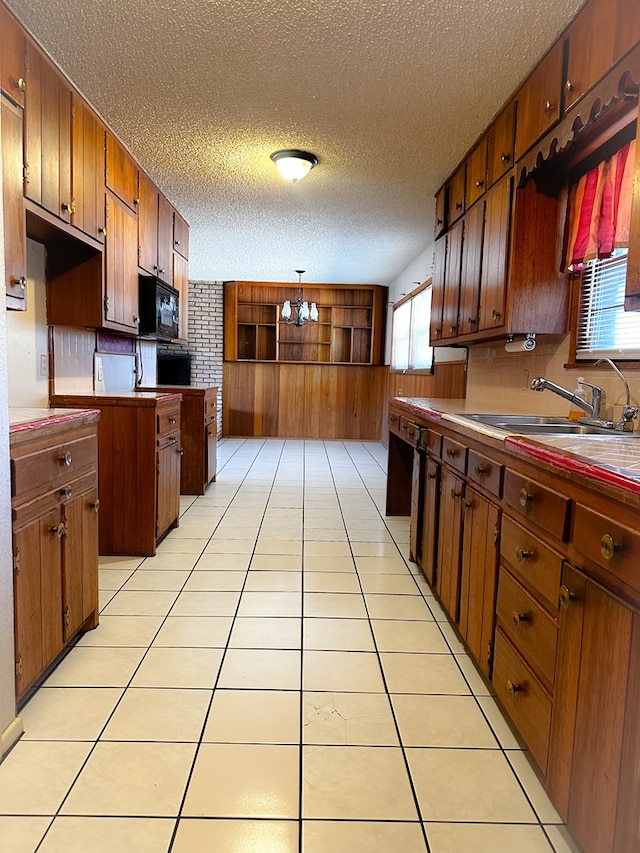 kitchen with sink, an inviting chandelier, hanging light fixtures, light tile patterned floors, and black appliances