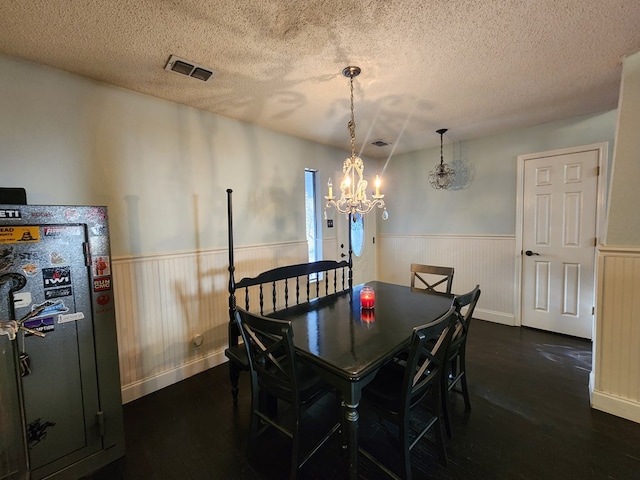 dining space featuring a wainscoted wall, dark wood finished floors, visible vents, a textured ceiling, and a chandelier