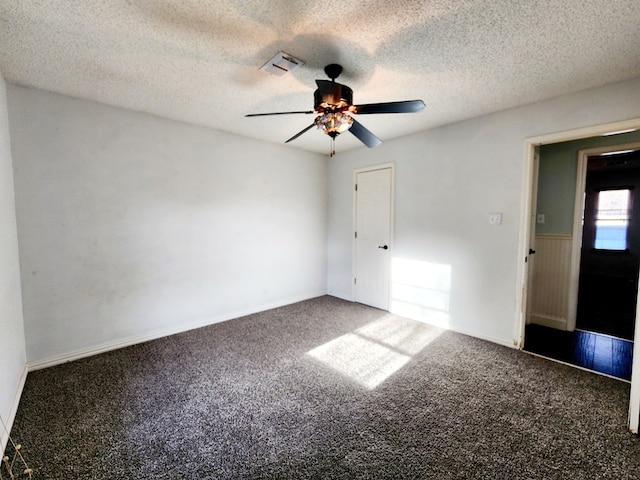 carpeted empty room featuring a textured ceiling, wainscoting, visible vents, and a ceiling fan