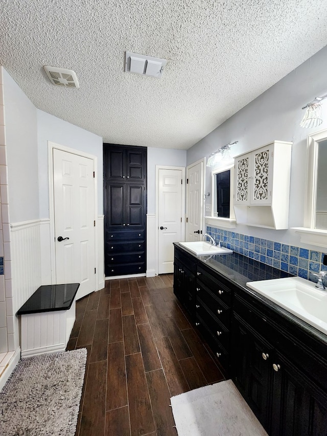 bathroom with a sink, visible vents, wood finished floors, and wainscoting