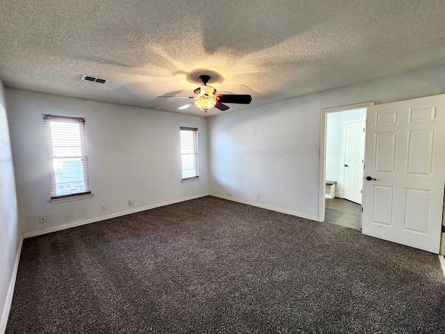 spare room with a ceiling fan, dark colored carpet, visible vents, and baseboards