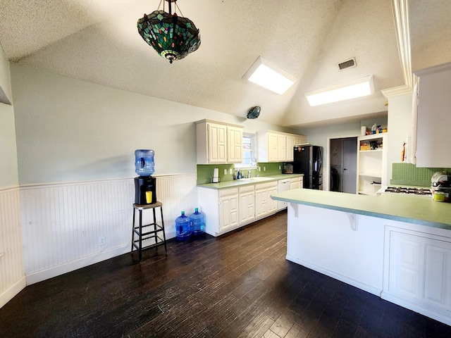 kitchen featuring visible vents, lofted ceiling, a wainscoted wall, dark wood-style flooring, and a peninsula