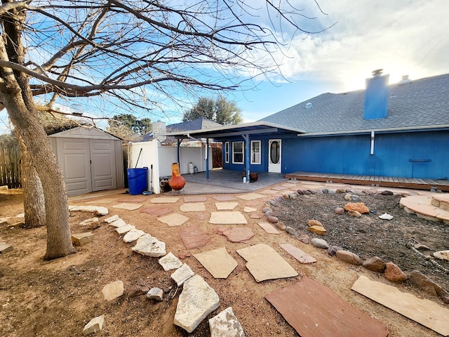 back of house with a patio, roof with shingles, fence, an outdoor structure, and a shed