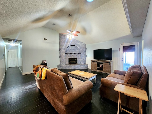 living room featuring a ceiling fan, lofted ceiling, wood-type flooring, a textured ceiling, and a fireplace