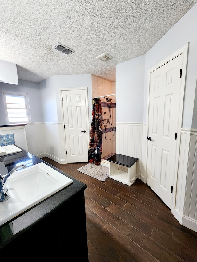 bathroom with a textured ceiling, a wainscoted wall, wood finish floors, visible vents, and a shower stall